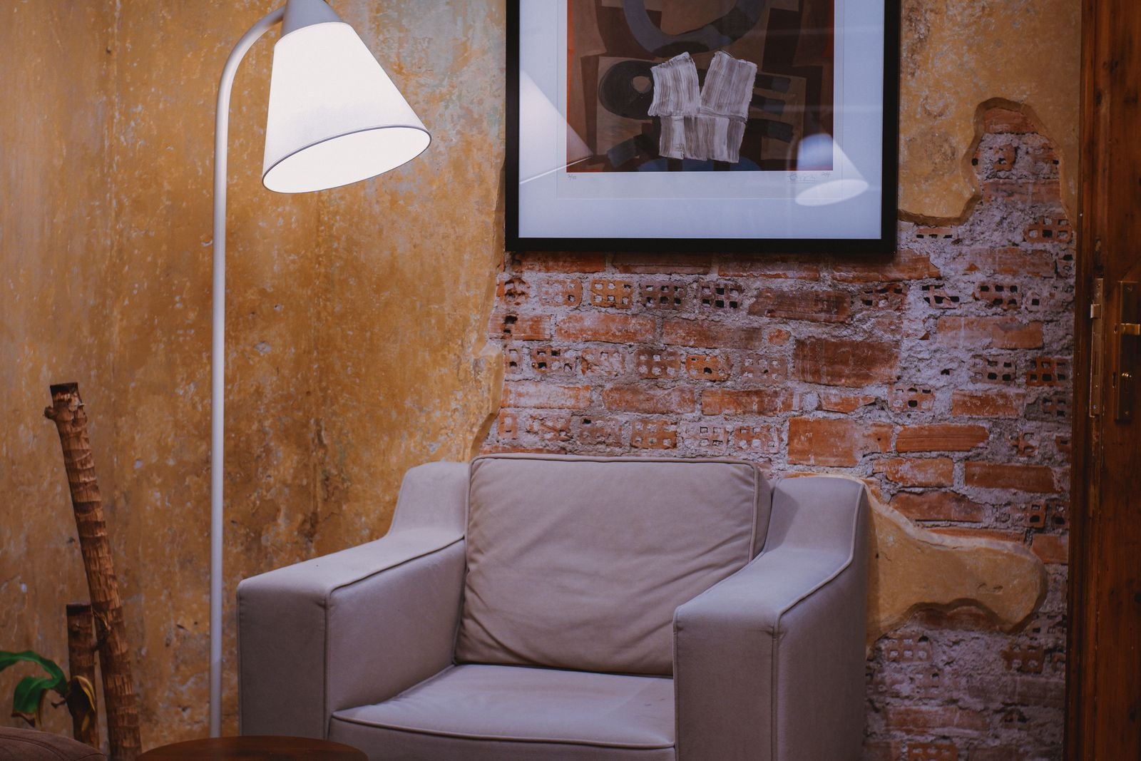 Cozy reading corner with a simple armchair, floor lamp and framed art against a brick wall