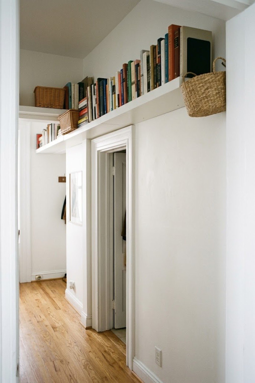 Long white floating shelf with books mounted above an apartment doorway