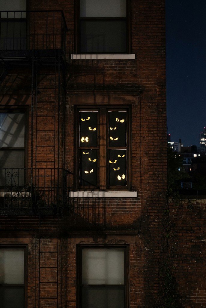 Dark window with glowing yellow eyes peeking out at night