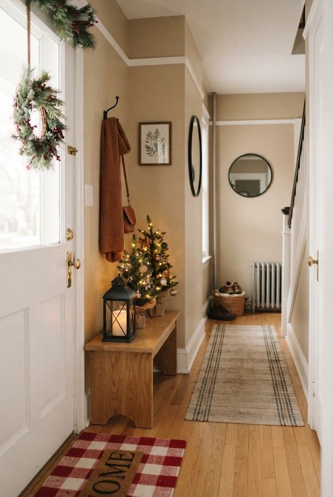 Narrow apartment entry with a wood bench, black lantern, mini lit tree and a red buffalo check doormat by the door