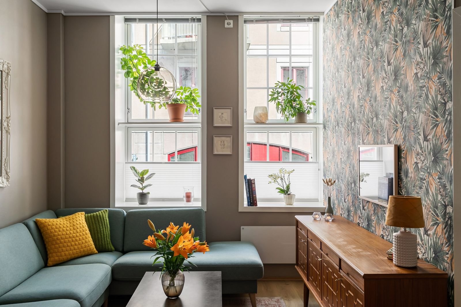 Small apartment living room with a teal sofa, plants and natural light