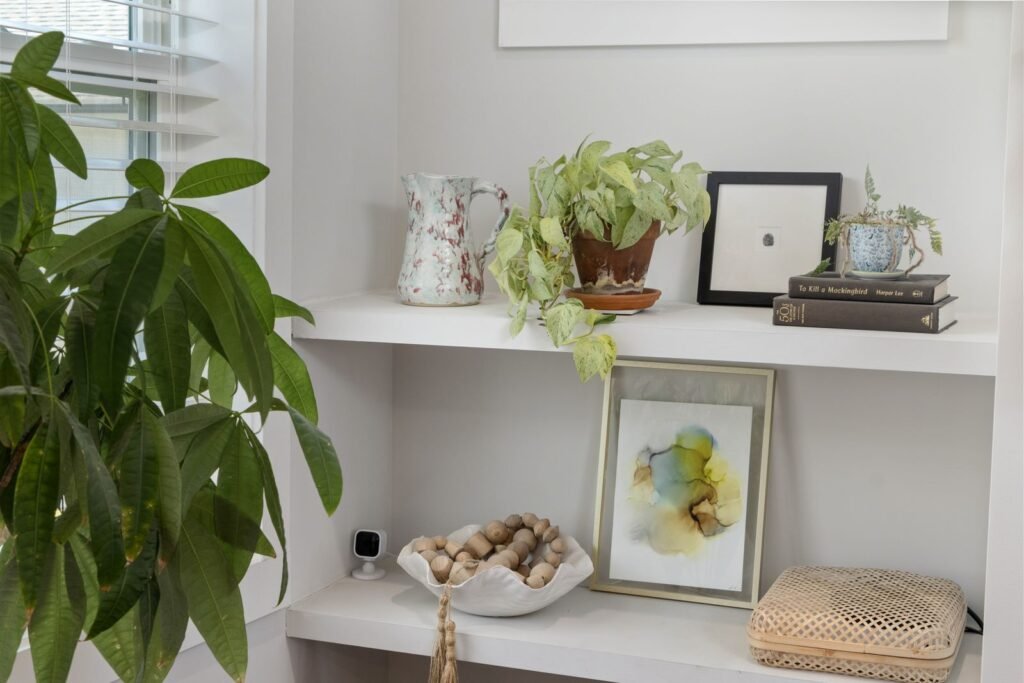 Bright styled shelf of thrifted home decor with framed art, vases, books and a trailing plant